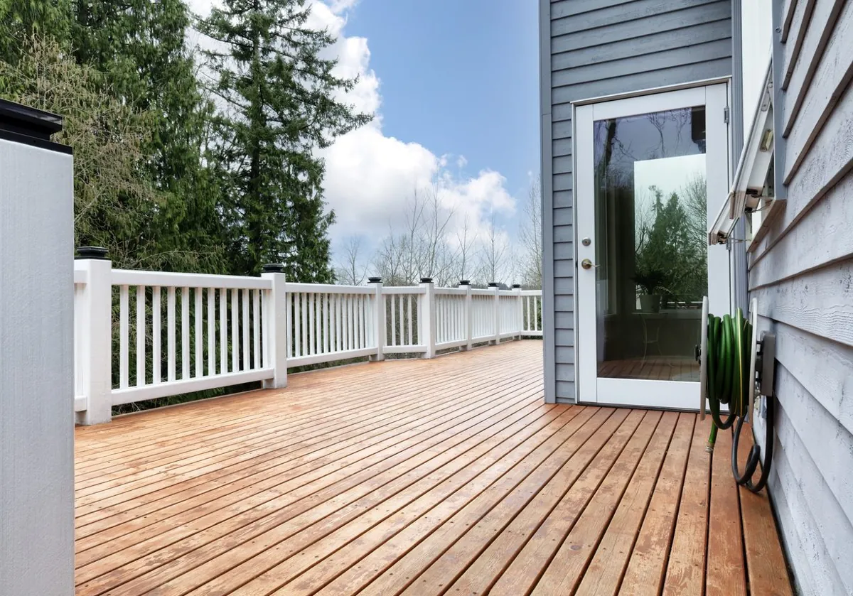 Freshly built natural wood deck with a white railing beside gray siding