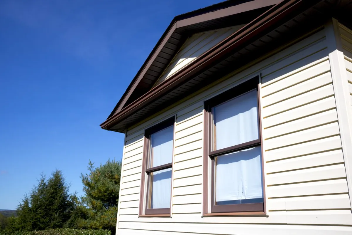 Two double-hung windows with brown trim on cream clapboard siding