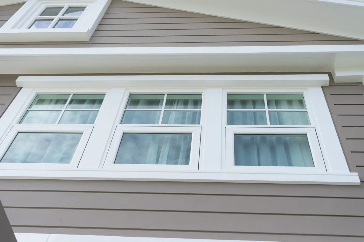 Three white double-hung windows with colonial grids on a sided home