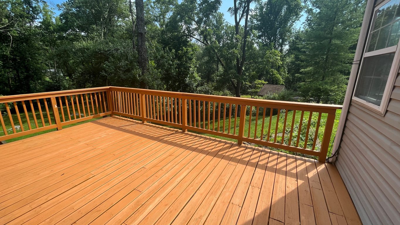 Cedar-stained wood deck and matching railing overlooking a wooded backyard
