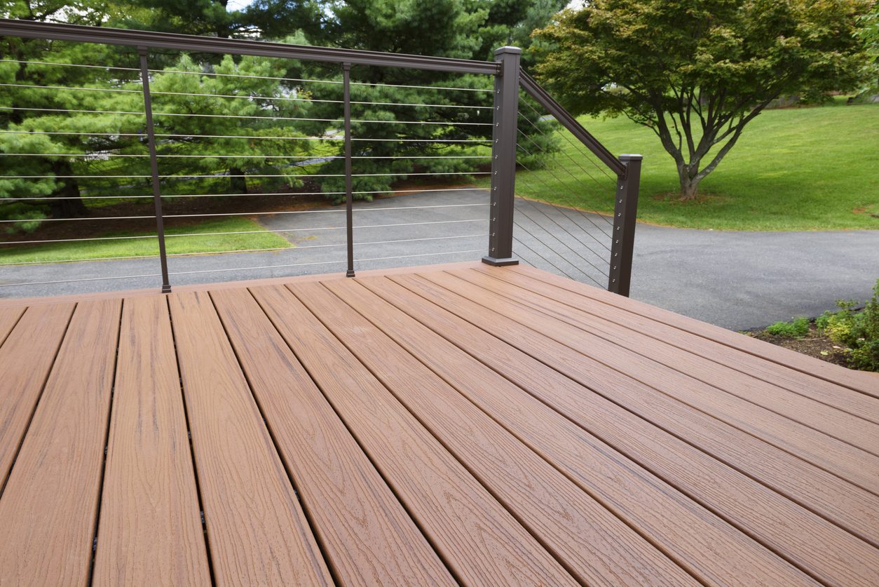 Brown composite deck with a black cable railing overlooking a landscaped yard