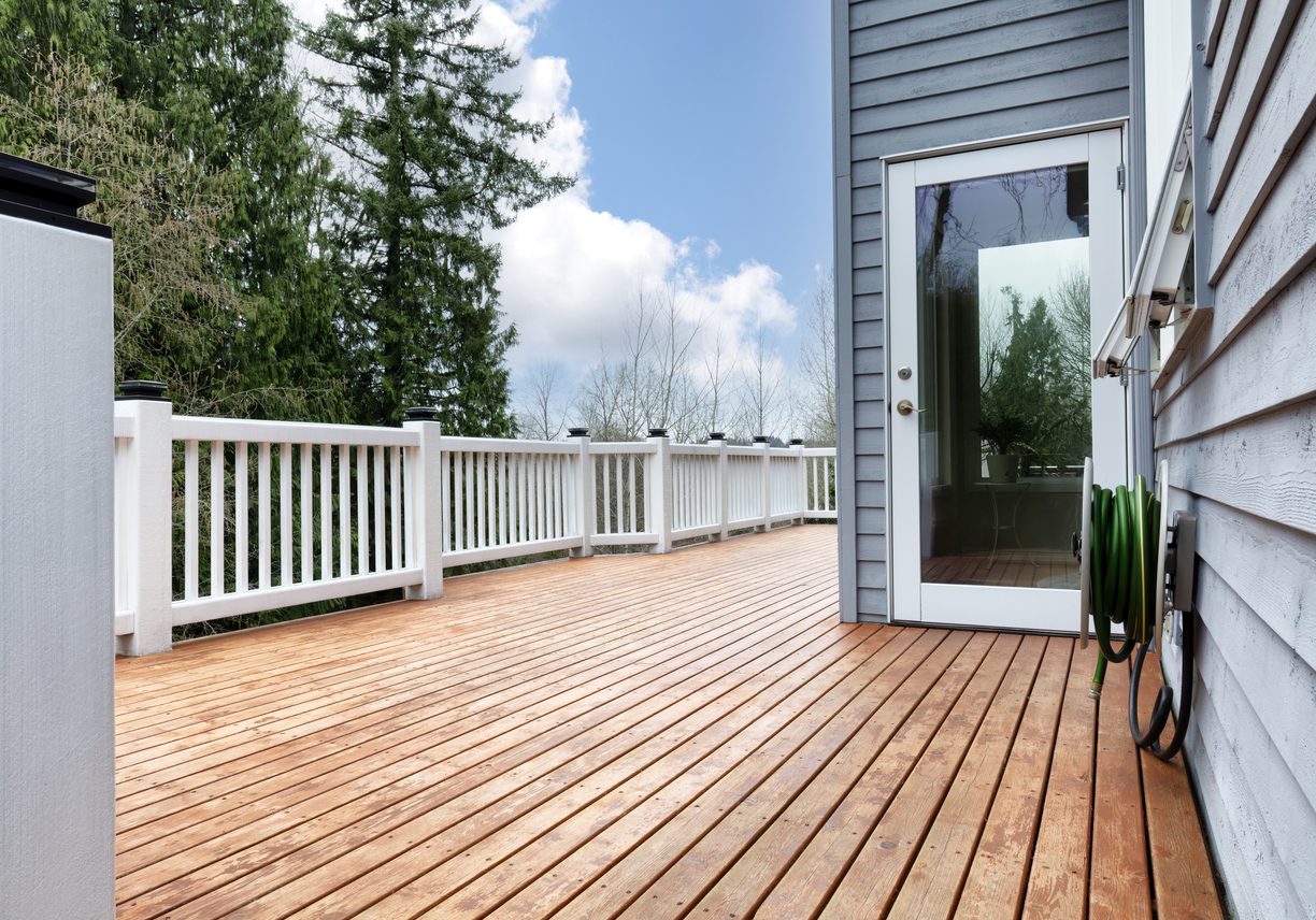 Freshly built natural wood deck with a white railing beside gray siding