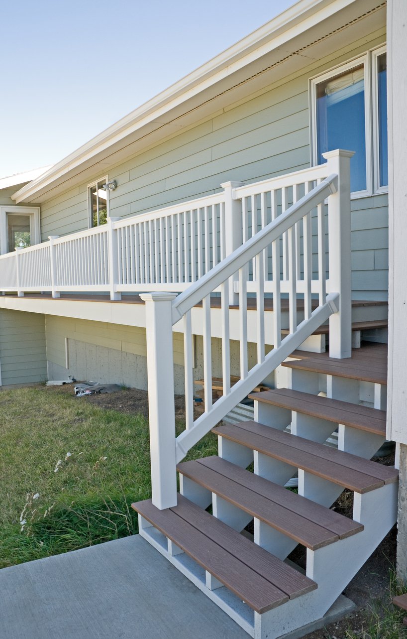 Raised deck with brown composite stairs and white railing on a green-sided home