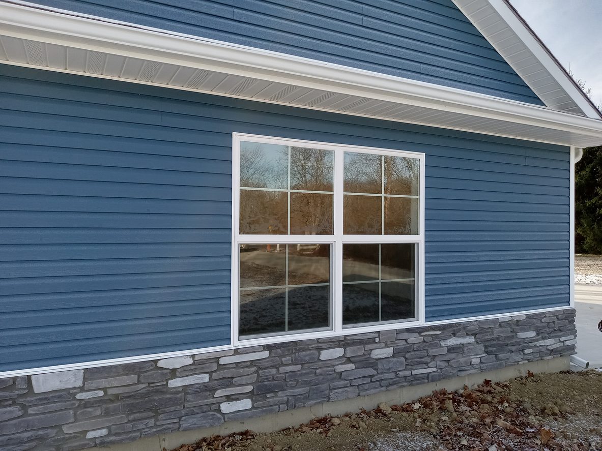Blue vinyl siding with a stone veneer wainscot and a white-trimmed window
