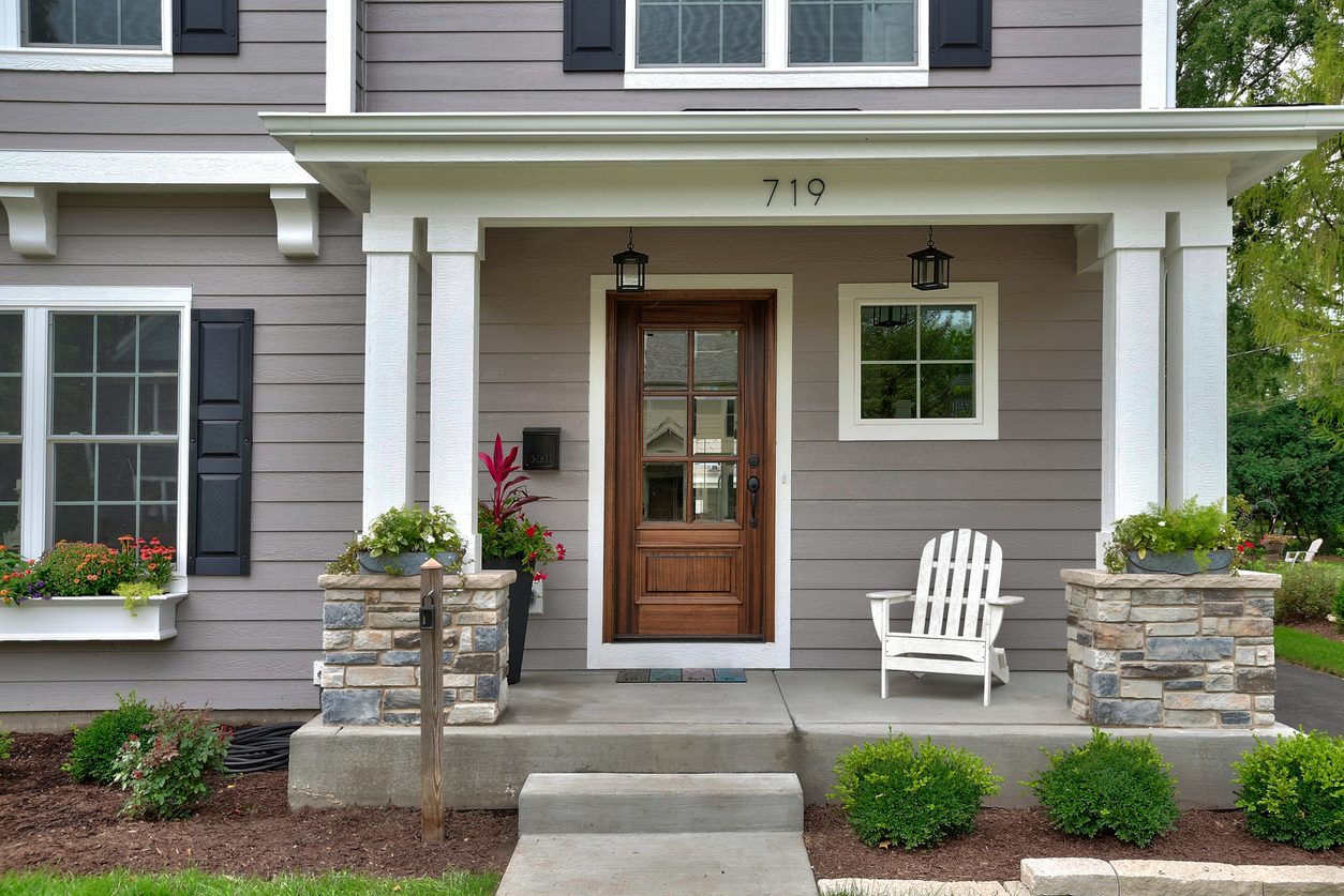 Warm gray craftsman porch with stone column bases and a wood front door