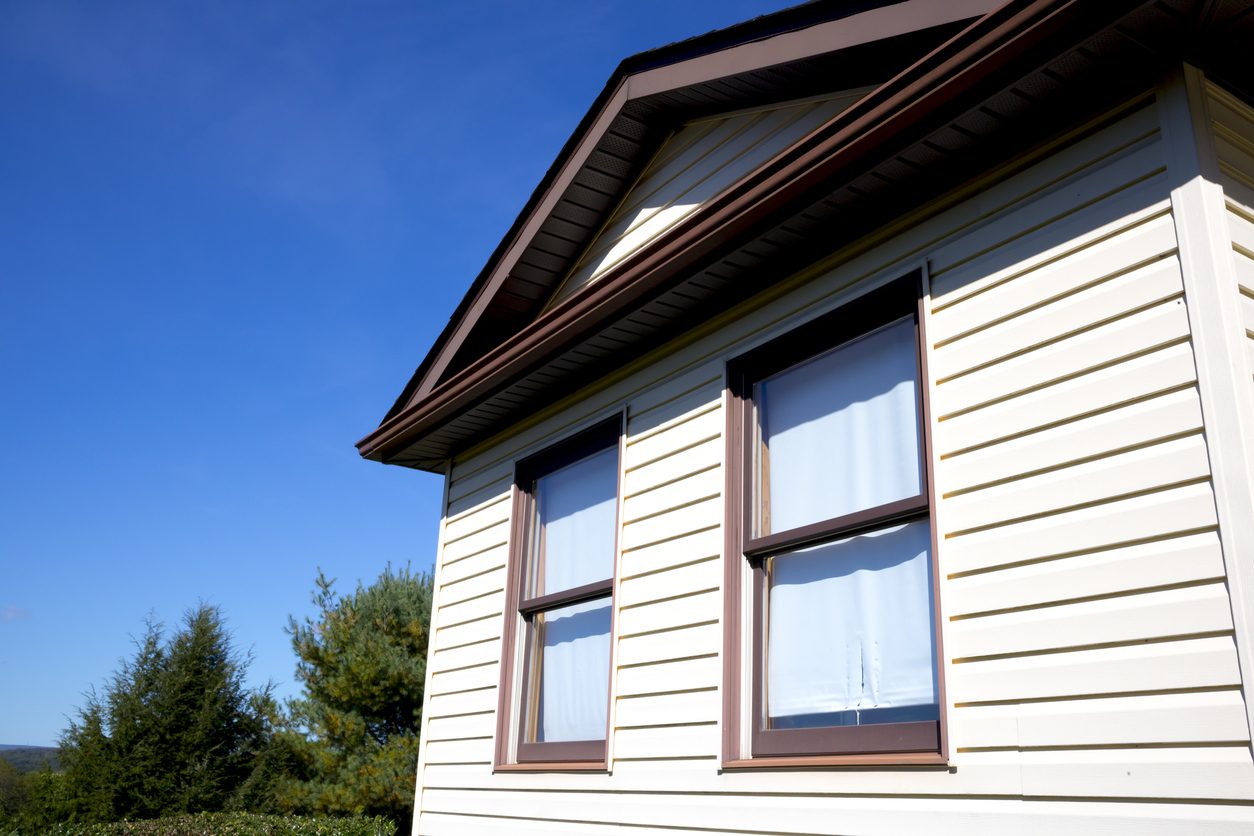 Two double-hung windows with brown trim on cream clapboard siding