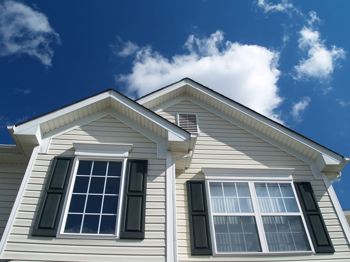 Two gabled windows with colonial grids and black shutters against a blue sky