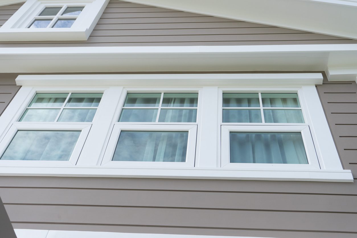 Three white double-hung windows with colonial grids on a sided home