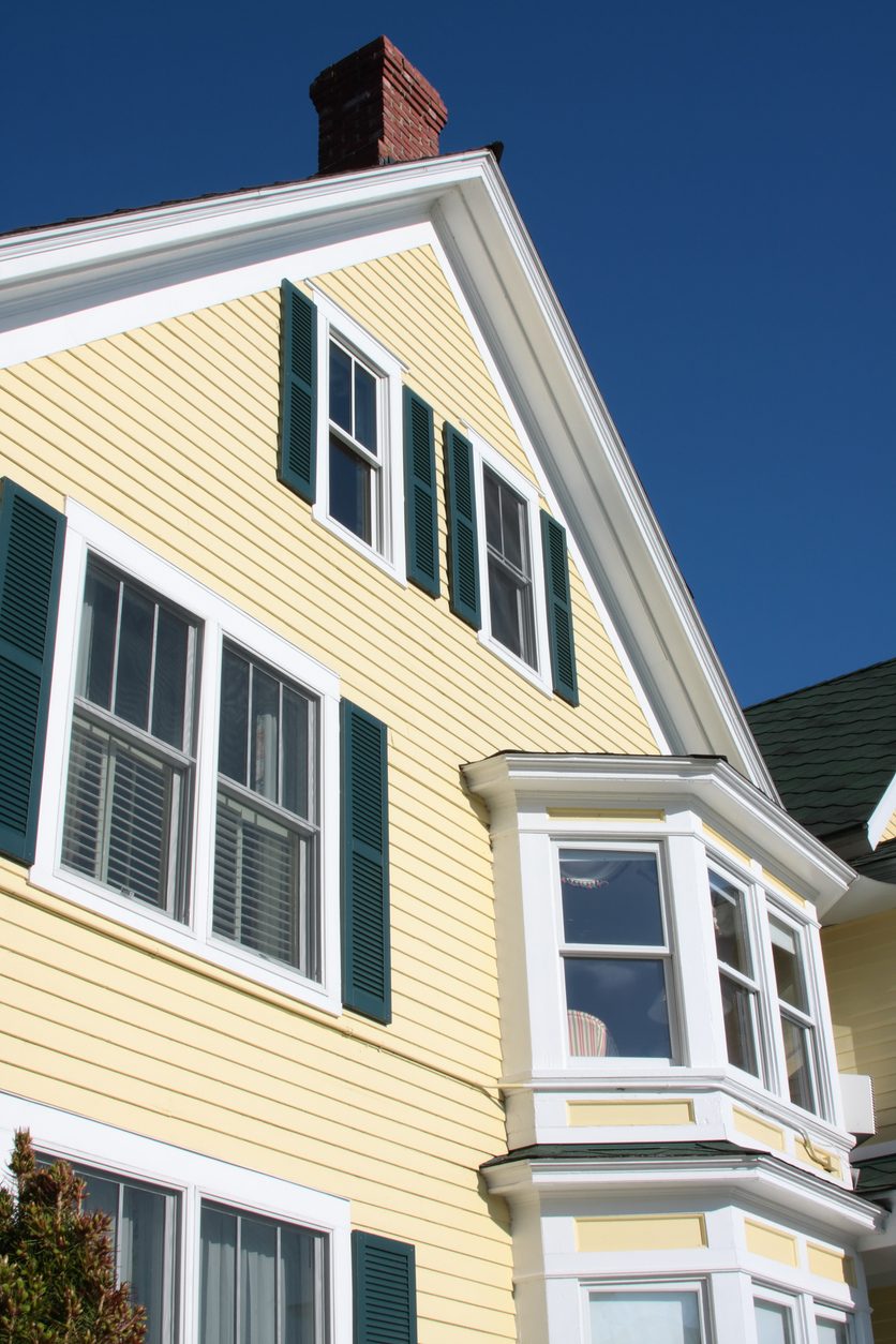 Yellow clapboard home with white double-hung windows, green shutters, and a bay window